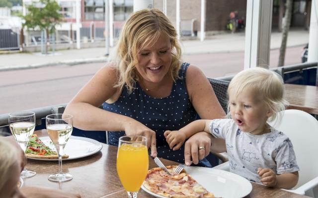 Kvinna skär upp pizza åt ett barn på uteserveringen vid Adlon Pizzeria & Sportsbar.