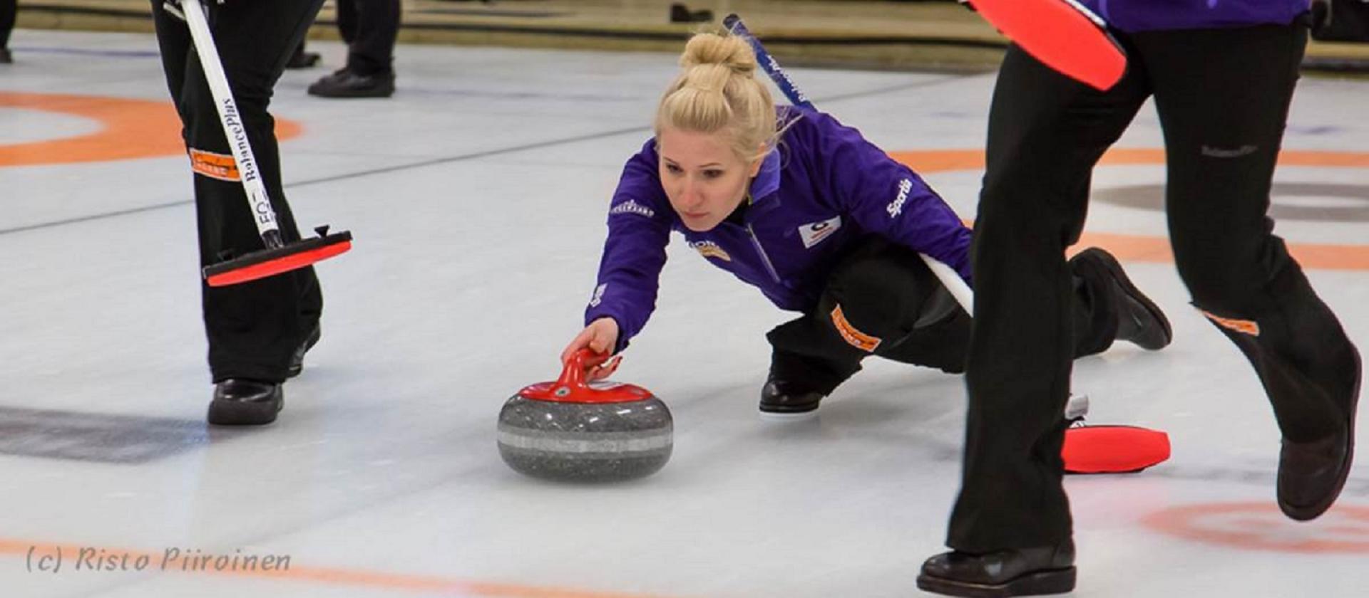 Kvinna som spelar curling i ishall på Åland.